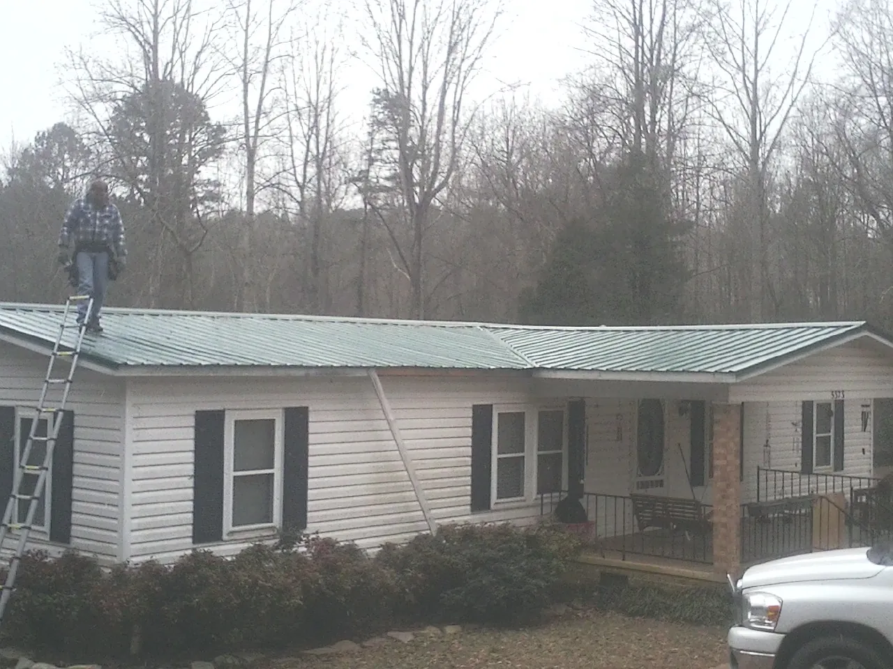 Worker on a ladder beside a new green metal roof on a ranch home in Kingsford Heights