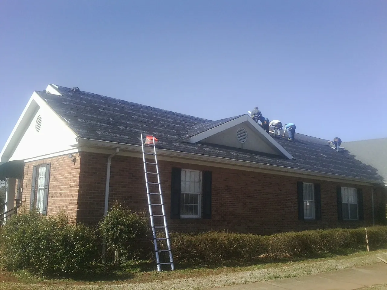 Crew tearing shingles off a brick ranch roof with a ladder set — Metal Roof Repair work by our crew in Kingsford Heights
