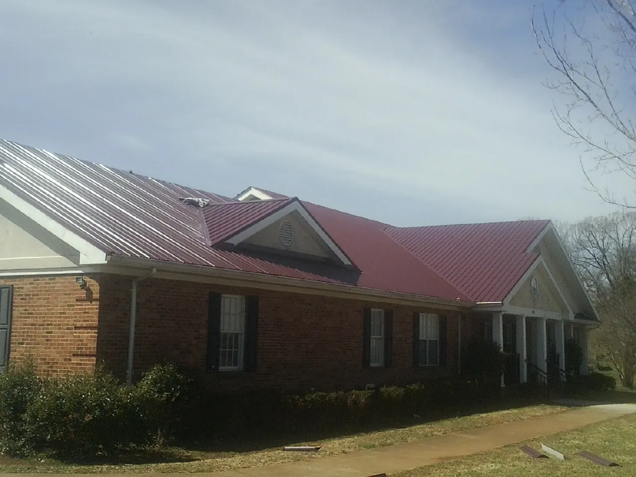 Red metal roof with gabled entries on a long brick building, from a Hail Damage Roof Repair job in Kingsford Heights