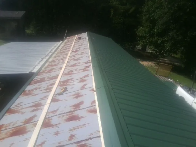 Old rusted panels beside newly installed green metal roofing — Wind Damage Roof Repair by Roofing Brothers in Kingsford Heights