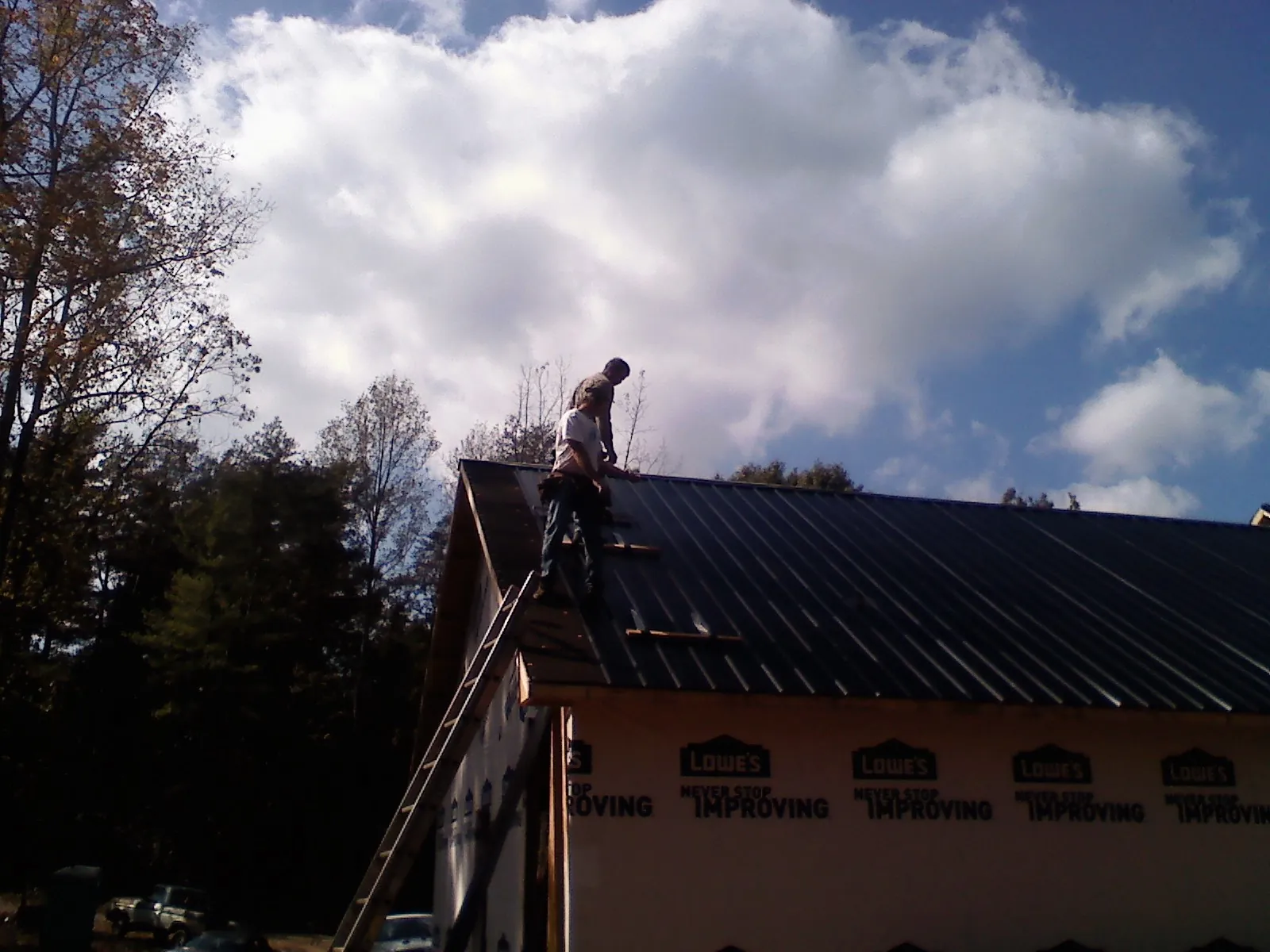 Roofer fastening dark metal panels high against a cloudy sky, from a Roof Inspection job in Kingsford Heights