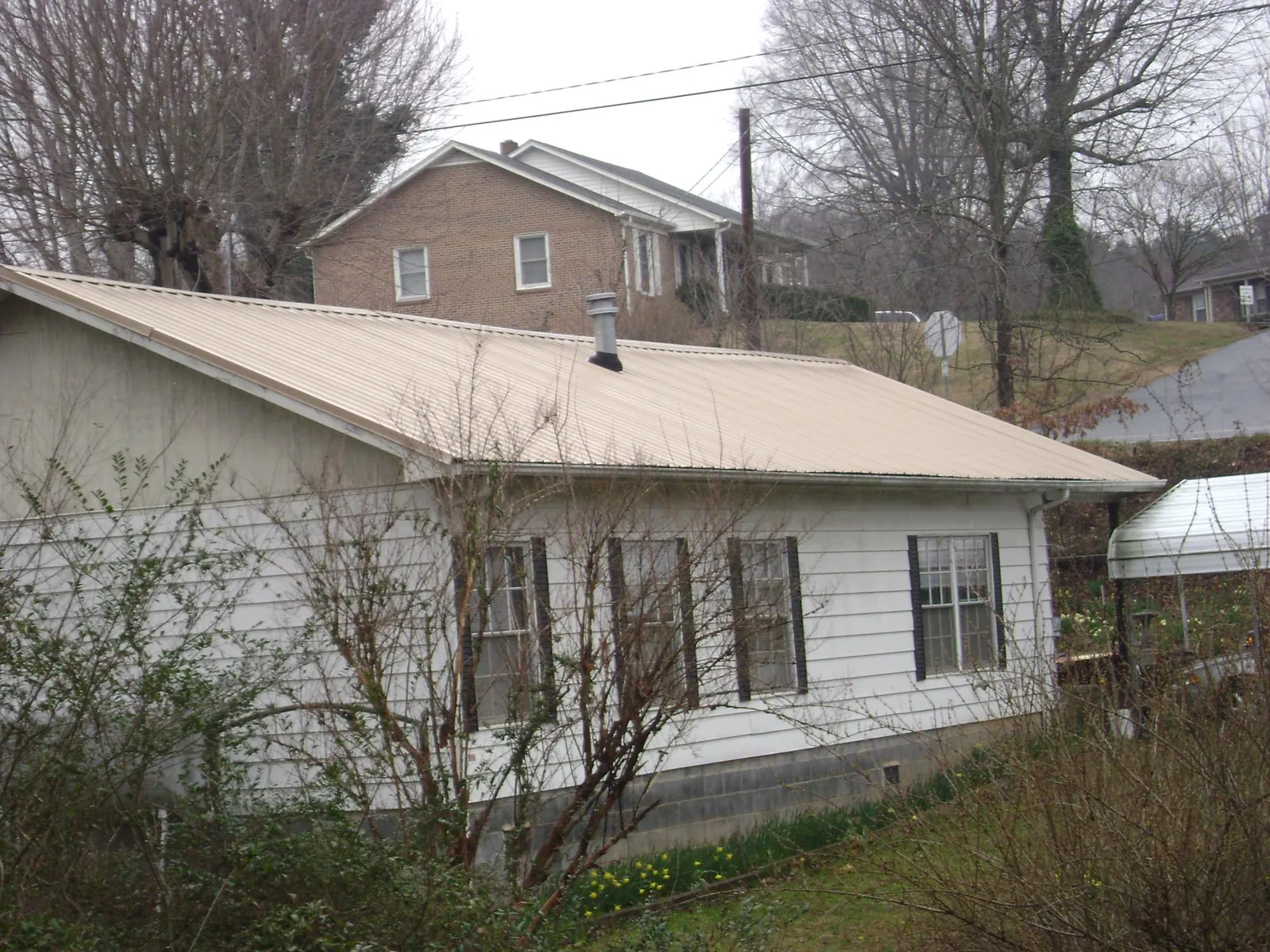 Tan metal roof on a white sided house set into a hillside — Commercial Roofing by Roofing Brothers in Kingsford Heights